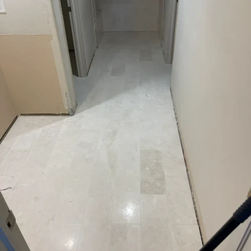 Continuous light-colored stone-look tile flooring installed flawlessly down a long residential hallway and into adjoining rooms in Colorado Springs, CO, by XCEL TILE.