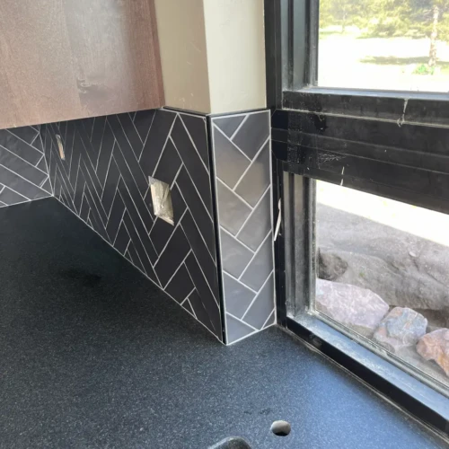 Detail view of professional edge finishing and trim protecting dark herringbone kitchen backsplash corners in Black Forest, CO, by XCEL TILE.