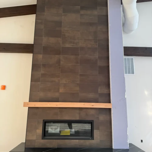 Floor-to-ceiling modern fireplace surround in Monument, CO, finished in dark, moody stone-look rectangular tile featuring a natural wood mantel by XCEL TILE.