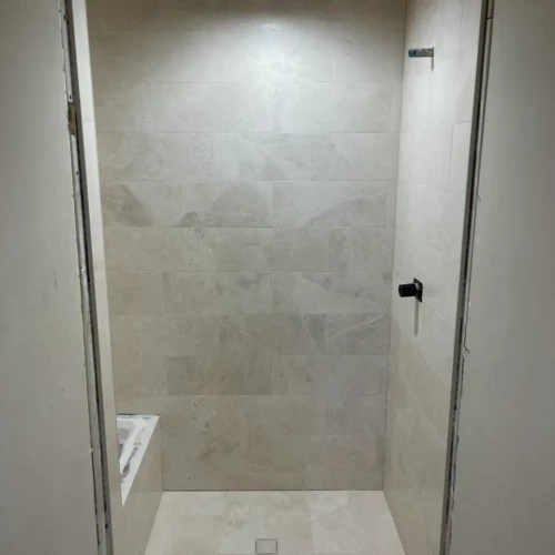 Finished light stone-look custom shower in Colorado Springs, CO, featuring a square center drain and a built-in tiled bench seating area in an alcove by XCEL TILE.