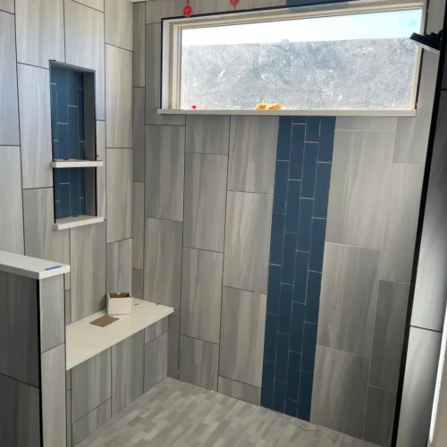 Walk-in shower under construction in Monument, CO, featuring light grey large-format tiles, a built-in bench, and a striking vertical band of dark blue accent tile by XCEL TILE.