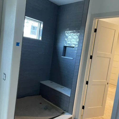 Tall walk-in shower enclosure in Larkspur, CO, finished in dark grey subway tile, featuring a built-in recessed niche, a window, and a white quartz bench by XCEL TILE.