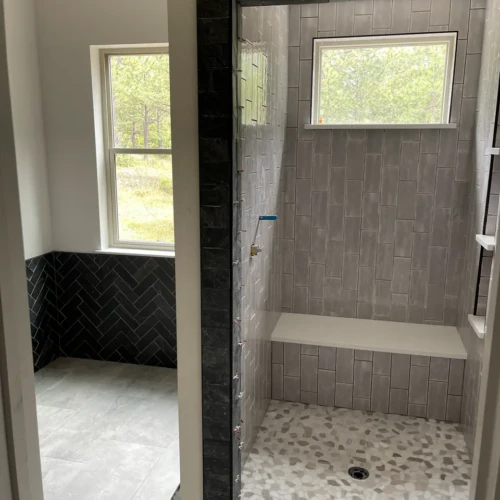 Finished walk-in shower featuring grey vertical subway tile, a built-in bench, and a natural stone pebble mosaic shower pan in Monument, CO, by XCEL TILE.