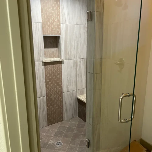 Finished walk-in shower featuring light wood-look wall tile, a vertical accent band of brown hexagon mosaics, a built-in niche, a bench, and a diagonally set stone-look floor in Parker, CO, by XCEL TILE.
