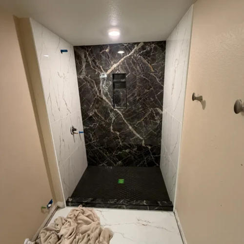 Luxury walk-in shower tile installation in Colorado Springs, CO, featuring large-format white marble-look walls, a dark veined accent wall, and black hex floor pan by XCEL TILE.