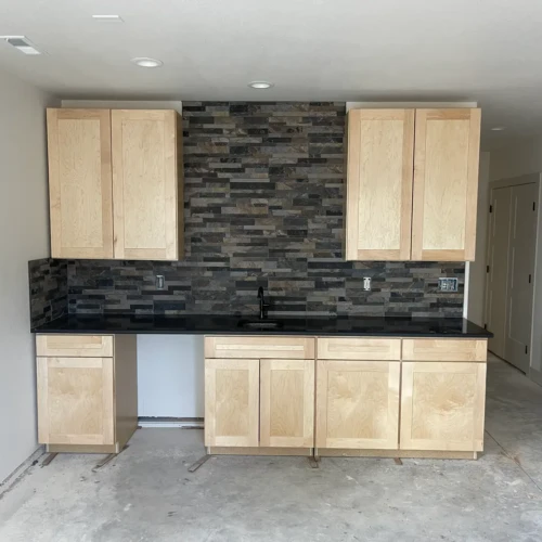 Residential wet bar under construction in Parker, CO, featuring light wood cabinetry, dark countertops, and a heavily textured dark slate stacked stone backsplash by XCEL TILE.