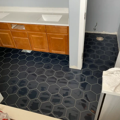 Dark blue hexagon tile in Monument, CO, installed seamlessly across a residential bathroom floor, running beneath a custom wood vanity by XCEL TILE.