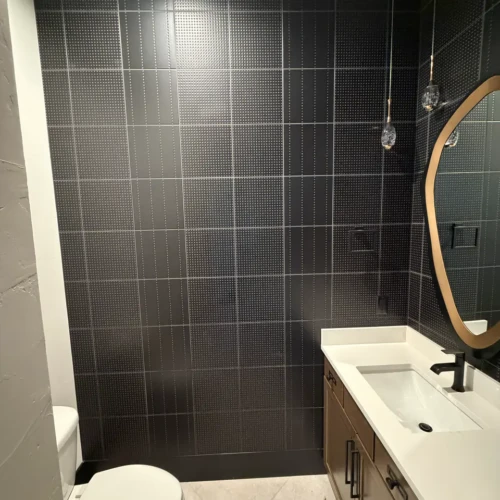Close-up of a bathroom vanity area in Colorado Springs, CO, highlighting a floor-to-ceiling installation of textured matte black square wall tiles by XCEL TILE.