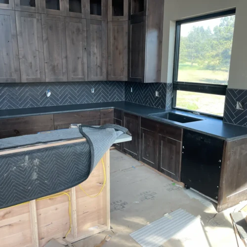 Complete kitchen in Black Forest, CO, featuring dark wood cabinetry and a sweeping dark grey herringbone pattern tile backsplash by XCEL TILE.