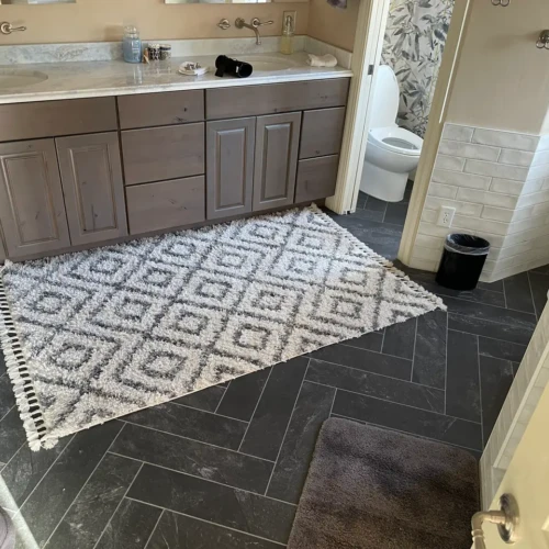 Master bathroom in Monument, CO, featuring dark grey slate porcelain tiles laid in a precise herringbone pattern alongside a rustic wood vanity by XCEL TILE.