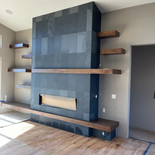 Wide view of a modern living room in Castle Rock, CO, featuring a massive custom fireplace wrapped in black slate tile, flanked by thick, natural wood floating shelves by XCEL TILE.