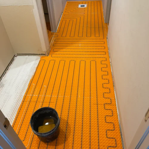 Bright orange uncoupling membrane with blue electric floor heating cables routed through it, laid out down a residential bathroom hallway in Colorado Springs, CO, by XCEL TILE.