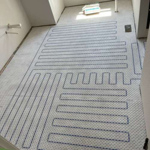 White uncoupling membrane with blue electric floor heating cables routed through it, laid out across a residential bathroom floor in Monument, CO, by XCEL TILE.