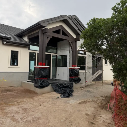 Custom home entrance under construction in Colorado Springs, CO, featuring large-format white porcelain slabs installed on the exterior facade alongside rustic timber columns by XCEL TILE.