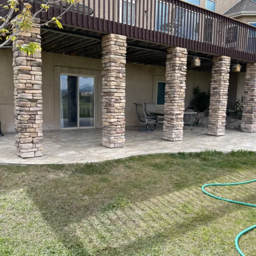 Wide view of a large covered outdoor patio in Peyton, CO, finished in durable stone-look porcelain floor tiles beneath a wooden deck by XCEL TILE.