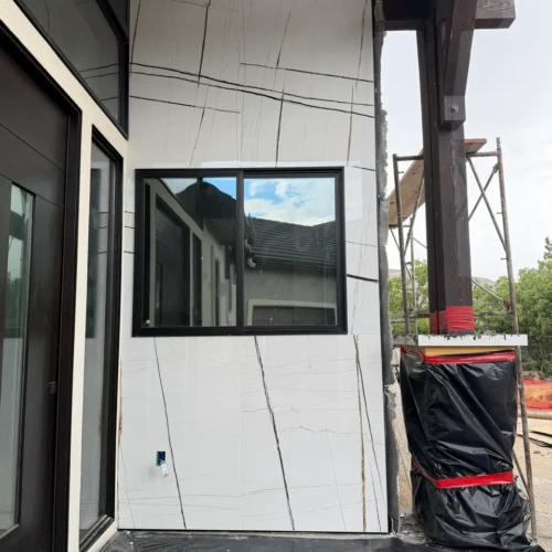 Close-up of exterior facade construction in Colorado Springs, CO, featuring white marble-look porcelain slabs meticulously cut and wrapped around a black window frame by XCEL TILE