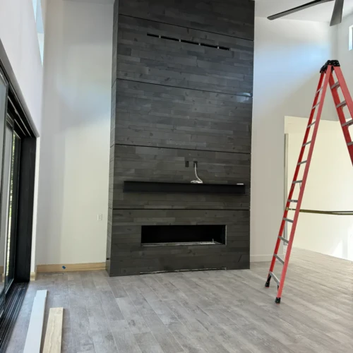 Modern living room in Black Forest, CO, featuring a tall floor-to-ceiling fireplace surround tiled with dark stacked horizontal porcelain planks by XCEL TILE.