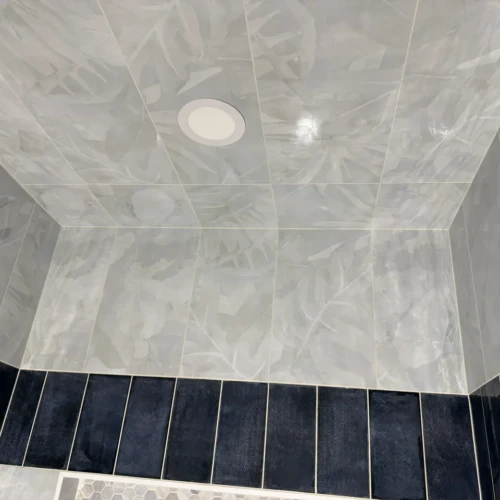 Looking up at a fully tiled shower ceiling in Manitou Springs, CO, featuring large-format light grey botanical pattern tiles, bordered by dark navy vertical accent tiles by XCEL TILE.