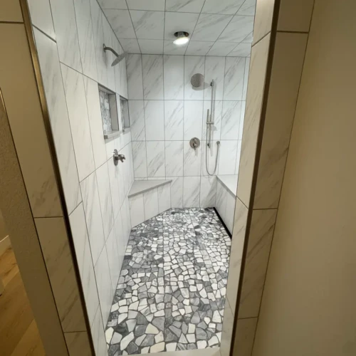 View through a doorway into a luxury wet room in The Broadmoor, CO, showcasing a fully tiled marble-look ceiling and custom pebble shower floor by XCEL TILE.