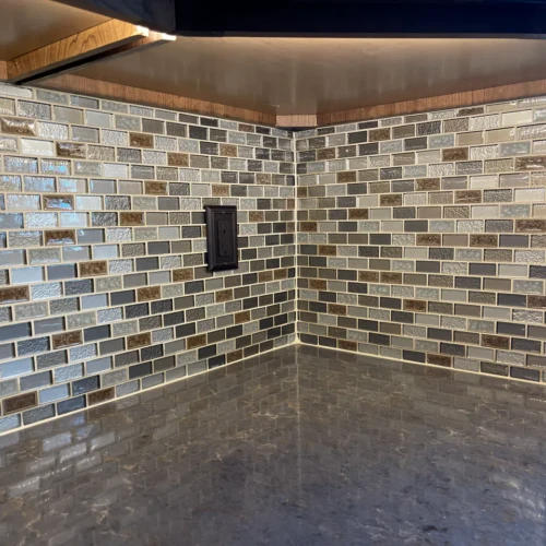 Close-up of a kitchen corner Colorado Springs, CO, featuring a multi-colored glass mosaic tile backsplash and perfectly cut dark outlet covers over a dark stone countertop by XCEL TILE.