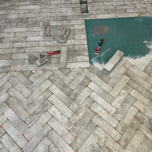 In-progress floor installation showing grey brick-look tiles being laid in a herringbone pattern over a green uncoupling membrane using orange spacers in Colorado Springs, CO, by XCEL TILE.