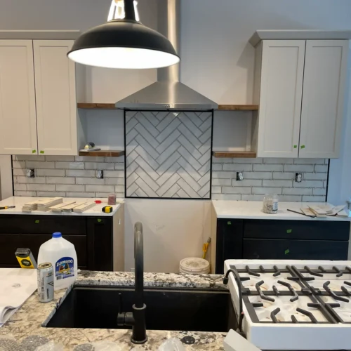 Kitchen remodel featuring a light grey herringbone tile accent wall framed beneath a stainless steel vent hood, centered between custom cabinetry and floating shelvesTall, multi-tiered custom shower niche built into a light grey subway tile wall, featuring a light herringbone tile backer and white quartz shelves in Monument, CO, by XCEL TILE.