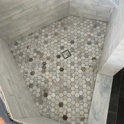 Walk-in shower floor pan in Monument, CO, featuring hexagon-shaped multi-toned marble mosaic tiles sloping toward a square drain by XCEL TILE.