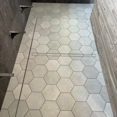 Completed large walk-in shower floor in Castle Rock, CO, featuring light grey hexagon tiles perfectly sloped toward a sleek linear drain by XCEL TILE.