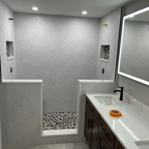 Modern master bathroom in Woodland Park, CO, featuring a walk-in shower with light grey hexagon wall tiles and a pebble mosaic floor by XCEL TILE.
