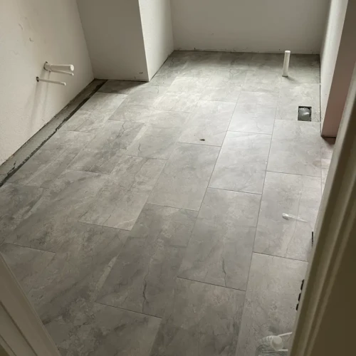 Continuous large-format grey stone-look tile flooring installed seamlessly throughout a residential bathroom and water closet in Monument, CO, by XCEL TILE.