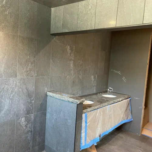 Bathroom vanity partition and surrounding walls in Black Forest, CO, finished in large-format charcoal stone-look porcelain tile by XCEL TILE.