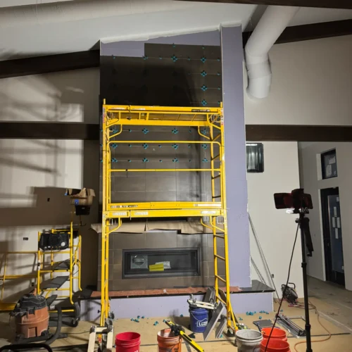 Large yellow scaffolding set up in front of a floor-to-ceiling fireplace during the installation of dark rectangular stone-look tiles in Monument, CO, by XCEL TILE.