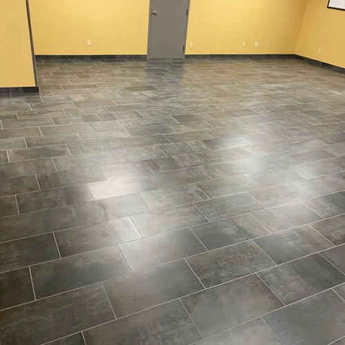 Expansive commercial office space showcasing perfectly laid grey floor tile with precise grout lines and matching baseboards in Colorado Springs, CO, by XCEL TILE.
