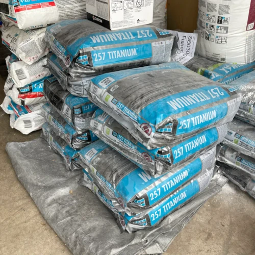 A large stack of blue Laticrete 257 Titanium lightweight thin-set mortar bags resting on a protective tarp.