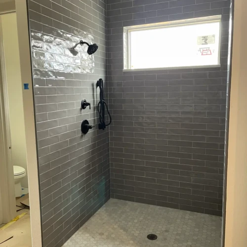 Finished custom walk-in shower in Larkspur, CO, featuring glossy grey subway tile walls, a white marble hexagon mosaic floor pan, and modern matte black fixtures by XCEL TILE.