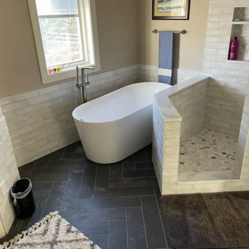 Luxury bathroom in Monument, CO, featuring a freestanding soaking tub next to a custom walk-in shower with white handmade-look subway tile and dark herringbone slate floors by XCEL TILE.