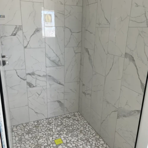 Modern walk-in shower featuring large-format white and grey marble-look porcelain wall tiles and a broken-pebble mosaic floor pan in Colorado Springs, CO, by XCEL TILE.