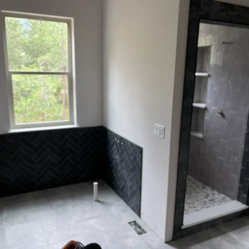 Master bathroom under construction featuring a black herringbone tile wainscoting accent wall and a walk-in shower framed in dark stone tile in Monument, CO, by XCEL TILE.