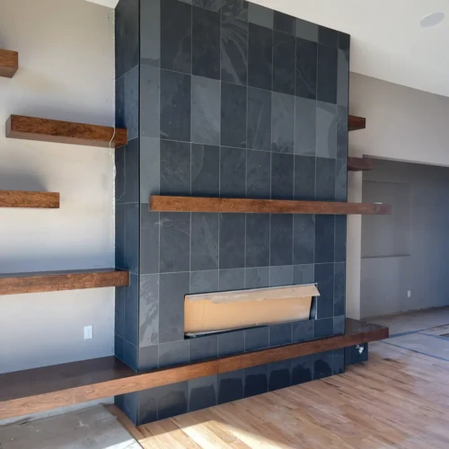 Floor-to-ceiling modern fireplace surround in Castle Rock, CO, finished in large-format dark black slate tile, seamlessly integrated with natural wood floating shelves and a wood mantel by XCEL TILE.