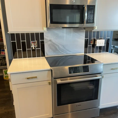 Close-up of a modern kitchen stove area featuring a seamless marble slab backsplash flanked by black vertical subway tiles with contrasting white grout in Colorado Springs, CO, by XCEL TILE.