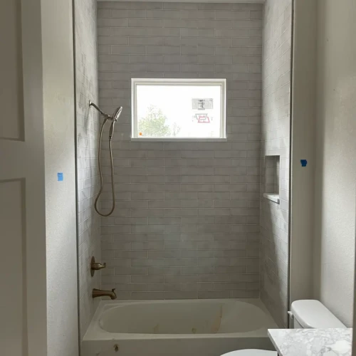 Bathtub shower surround tiled to the ceiling with light grey subway tile, featuring a built-in storage niche and warm antiqued brass plumbing fixtures in Parker, CO, by XCEL TILE.