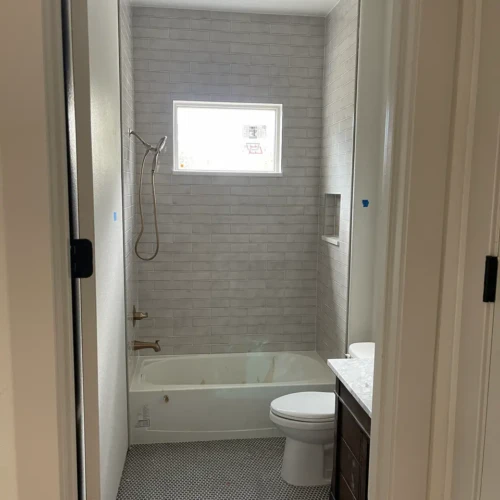 Residential bathroom in Parker, CO, featuring a light grey subway tile bathtub surround and a high-contrast dark penny round mosaic tile floor by XCEL TILE.