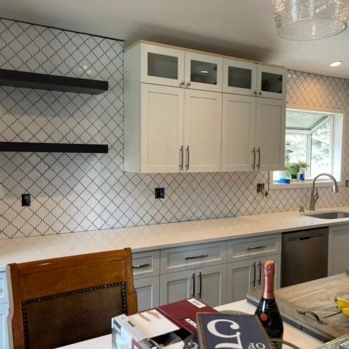 Wide view of a modern kitchen remodel in Monument, CO, showing a completed white arabesque tile backsplash extending to the ceiling behind dark floating shelves by XCEL TILE.