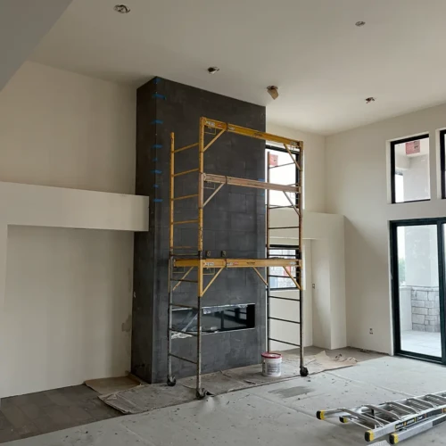 Scaffolding set up in front of a floor-to-ceiling modern fireplace surround finished in dark, large-format matte tile in a Colorado Springs home by XCEL TILE.