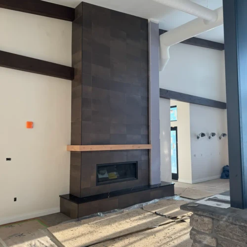 Completed dark stone-look floor-to-ceiling fireplace surround in Monument, CO, with a natural wood mantel in a modern, bright residential living space by XCEL TILE.