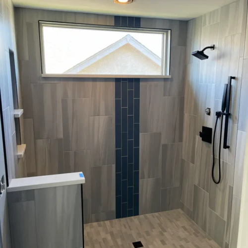 Completed modern walk-in shower in Monument, CO, featuring light grey tile, a dark blue vertical accent band, and sleek matte black plumbing fixtures by XCEL TILE.