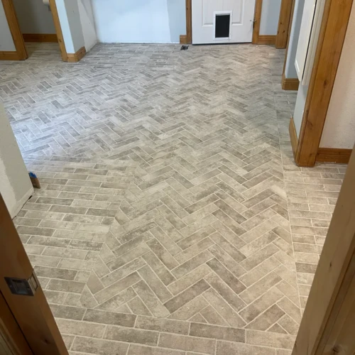 Custom mudroom flooring featuring weathered grey brick-look porcelain tiles installed in a classic herringbone pattern with bordered edges in Colorado Springs, CO, by XCEL TILE.