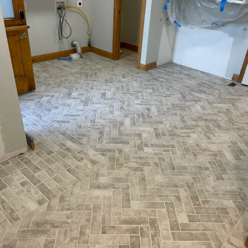 Custom mudroom flooring featuring weathered grey brick-look porcelain tiles installed in a classic herringbone pattern with bordered edges in Colorado Springs, CO, by XCEL TILE.