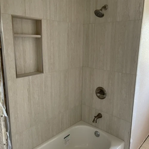 Finished bathtub and shower surround in Monument, CO, featuring vertical, neutral light-grey stone-look tile and a built-in recessed storage niche by XCEL TILE.