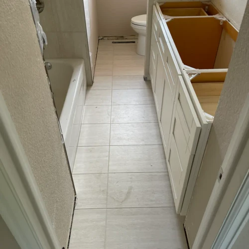 Light neutral square tile flooringin Monument, CO, installed in a residential bathroom, running alongside a bathtub and under a custom double vanity under construction by XCEL TILE.
